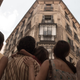 A family, photographed from the back, stares up at the windows of their apartment building.